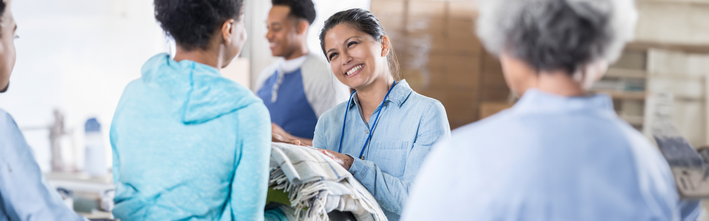 a person at a shelter smiling handing blankets to another person