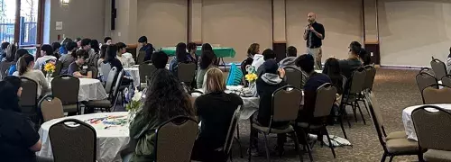 room full of youth sitting at tables listening to a speaker